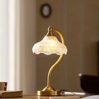 This Clérachic lamp glowing on a wooden table against a warm brown wall, its frosted shade lit softly from within.