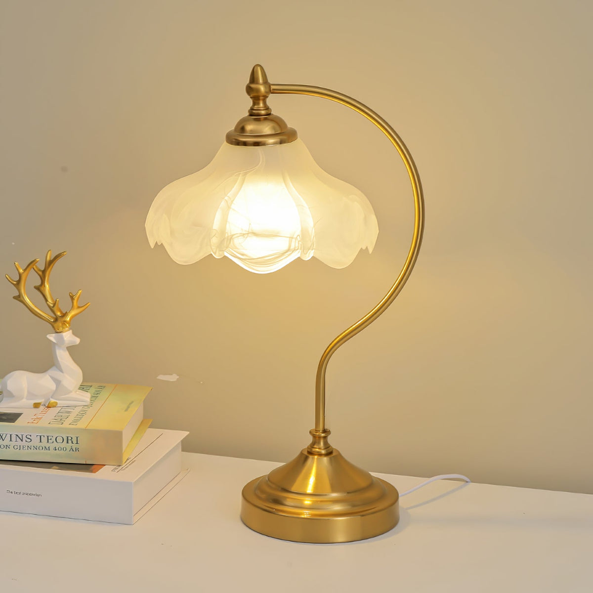 This Clérachic lamp lit warm on a white shelf, with a white deer figure and a stack of books against a golden wall.