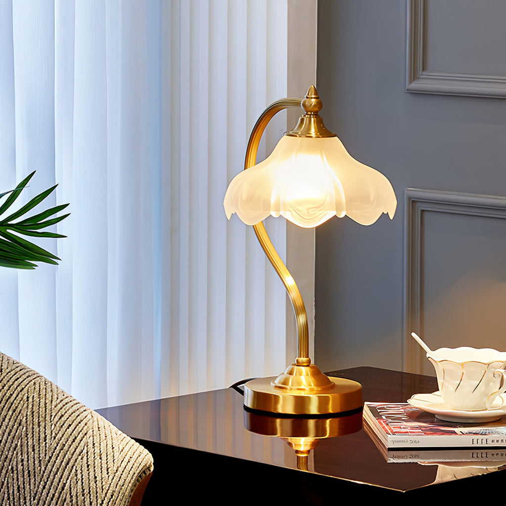A Clérachic lamp on a polished dark table by a window with sheer curtains, a teacup, magazines and a striped cushion beside it.