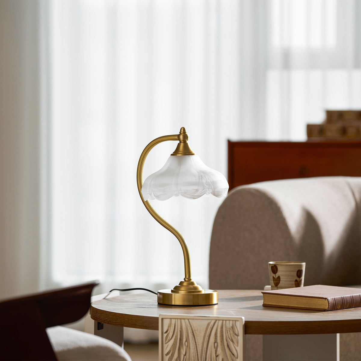 A Clérachic lamp with its frosted shade unlit, on a round table with a book and a mug, in a bright room by a window.