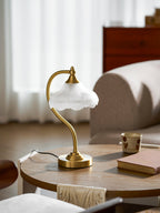 Side view of this Clérachic lamp on a round wooden table, with its black cord trailing across the top and a book and mug nearby.