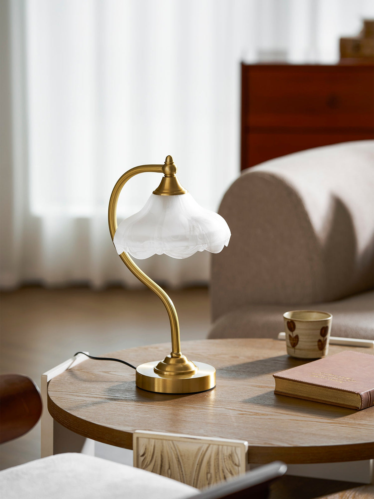 Side view of this Clérachic lamp on a round wooden table, with its black cord trailing across the top and a book and mug nearby.