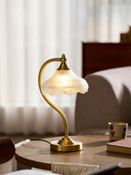 This Clérachic lamp switched on, its warm glow showing through the scalloped glass, on a wooden table by sheer curtains.