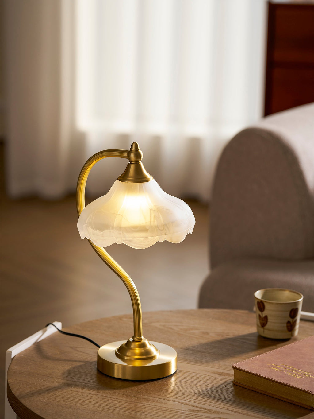 Closer view of this Clérachic lamp lit on a round wooden table, the frosted glass edge glowing against a grey sofa.