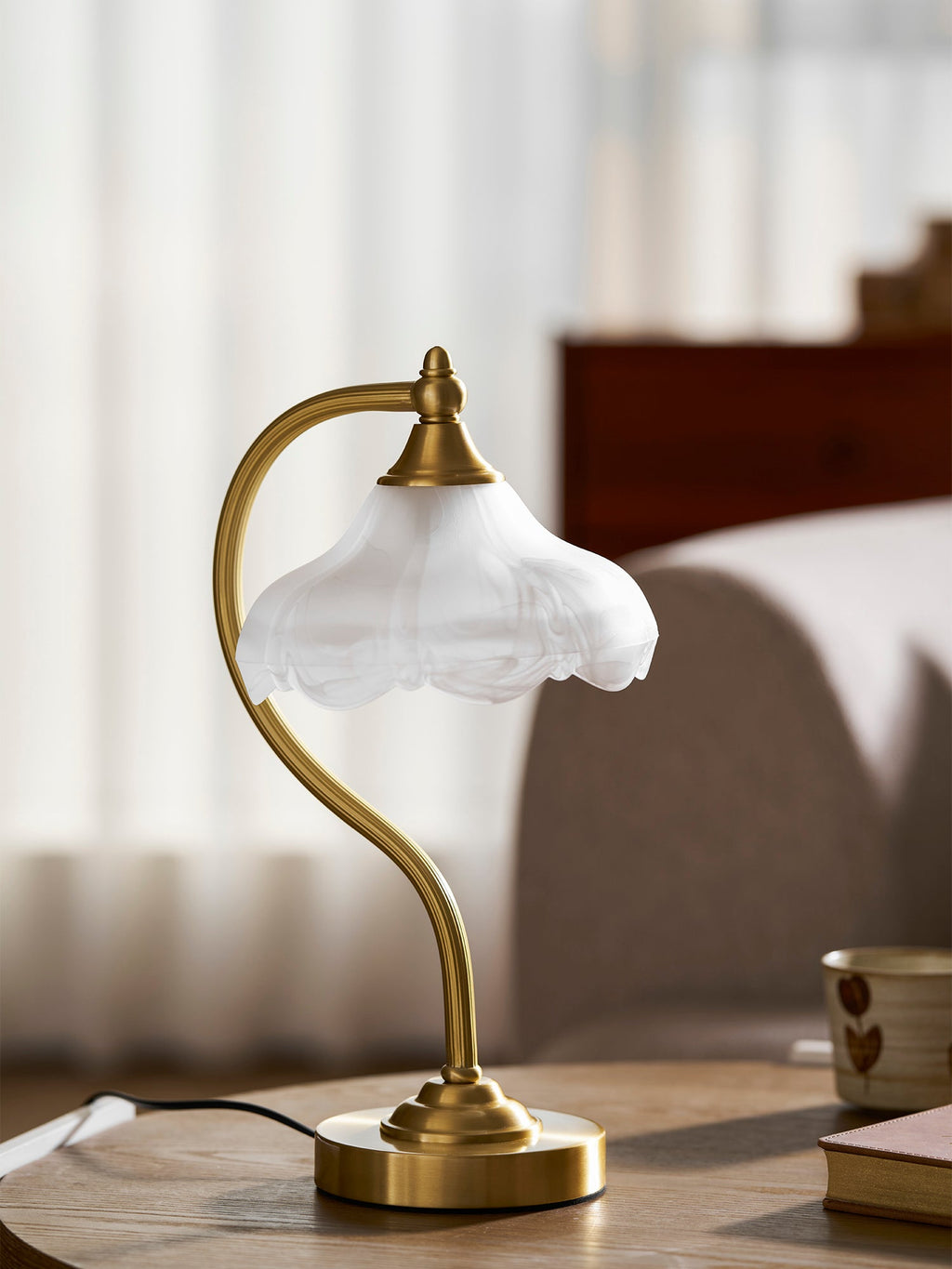 Close view of the scalloped frosted shade and the curved gold arm of this Clérachic lamp, unlit, on a wooden table.