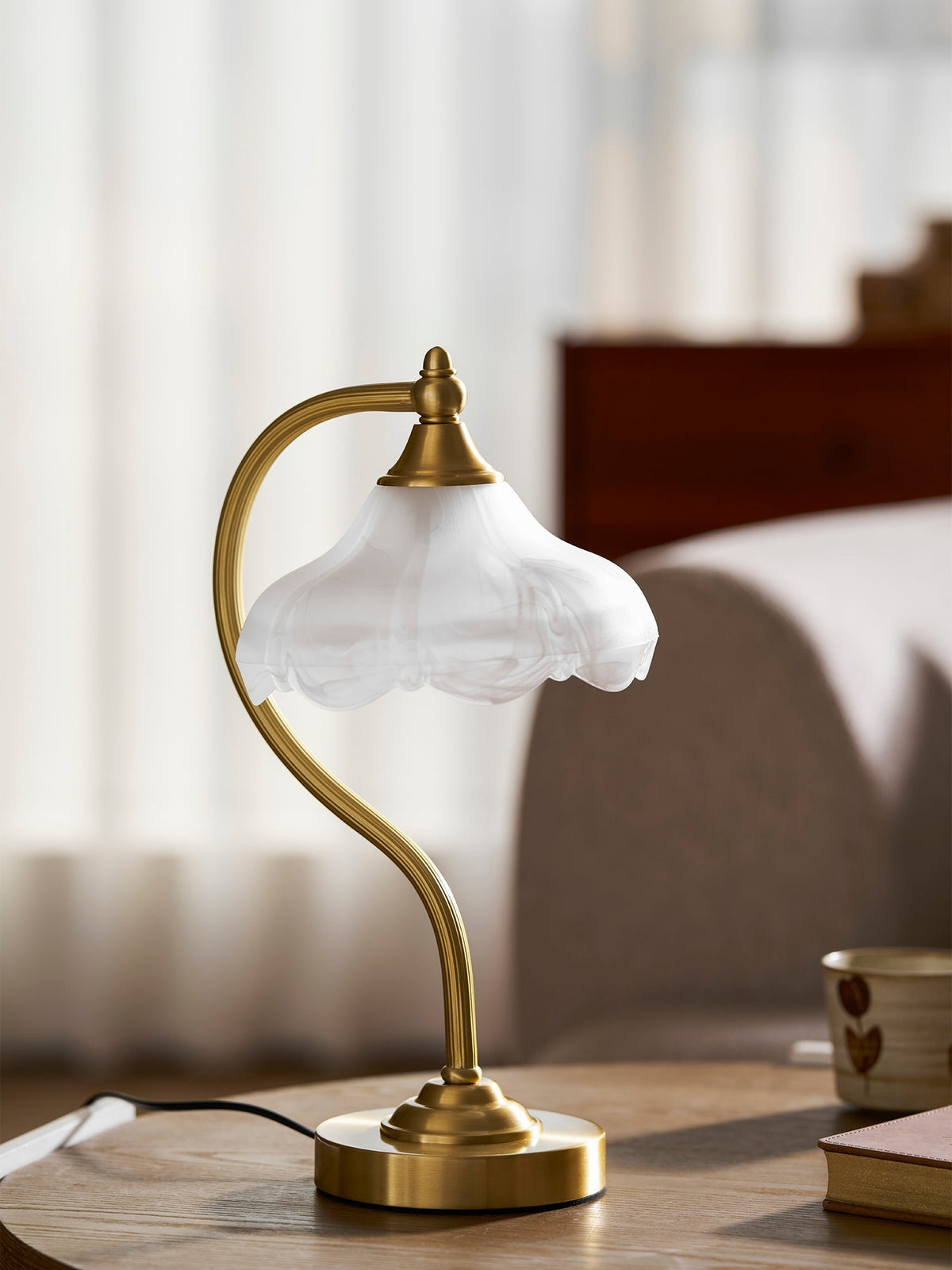 Close view of the scalloped frosted shade and the curved gold arm of this Clérachic lamp, unlit, on a wooden table.