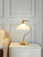 This Clérachic lamp glowing on a white bedside cabinet against a pale panelled wall, with a cream armchair at the left.