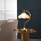 A Clérachic lamp lit on a round gold side table, beside a taupe tub chair and a deep navy wall.