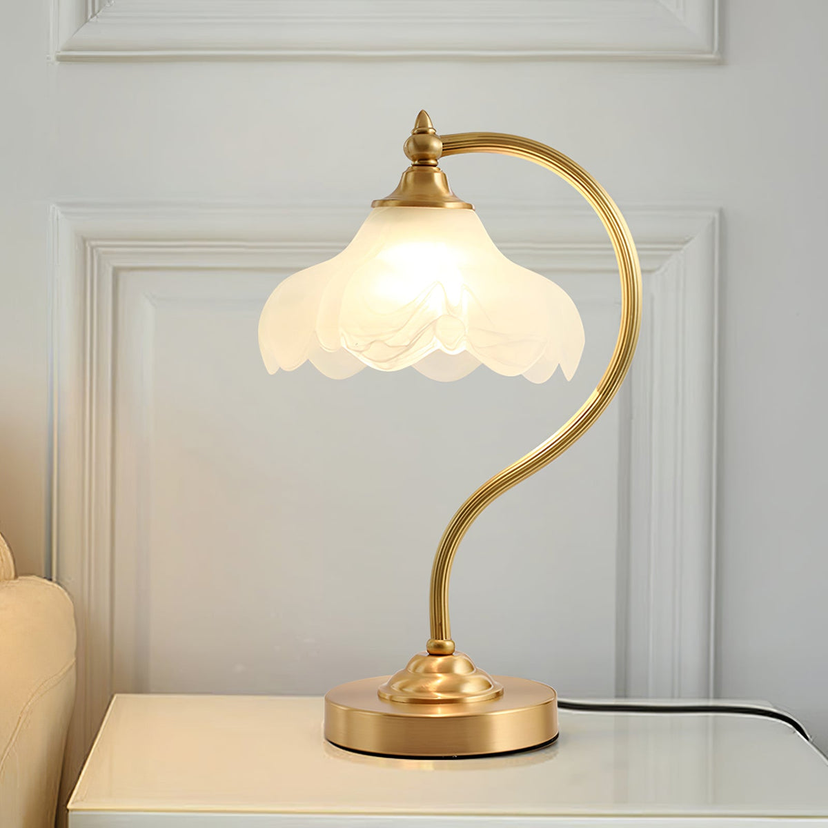 Wider view of this Clérachic lamp on a white cabinet, the scalloped shade glowing in front of a white panelled wall.