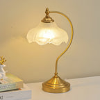 Close view of the scalloped glass shade and the round gold base of this Clérachic lamp, lit warm on a white shelf.