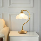 This Clérachic lamp lit on a white bedside cabinet beside a cream chair, in front of a white panelled wall.