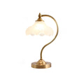 This Clérachic lamp softly lit on white, with its frosted shade glowing and a wide round brass base below.