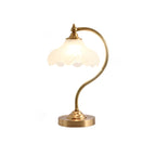 This Clérachic lamp softly lit on white, with its frosted shade glowing and a wide round brass base below.