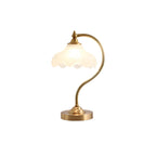 A Clérachic lamp on a white backdrop, its scalloped glass lit palely above a slim curved arm and a small gold base.