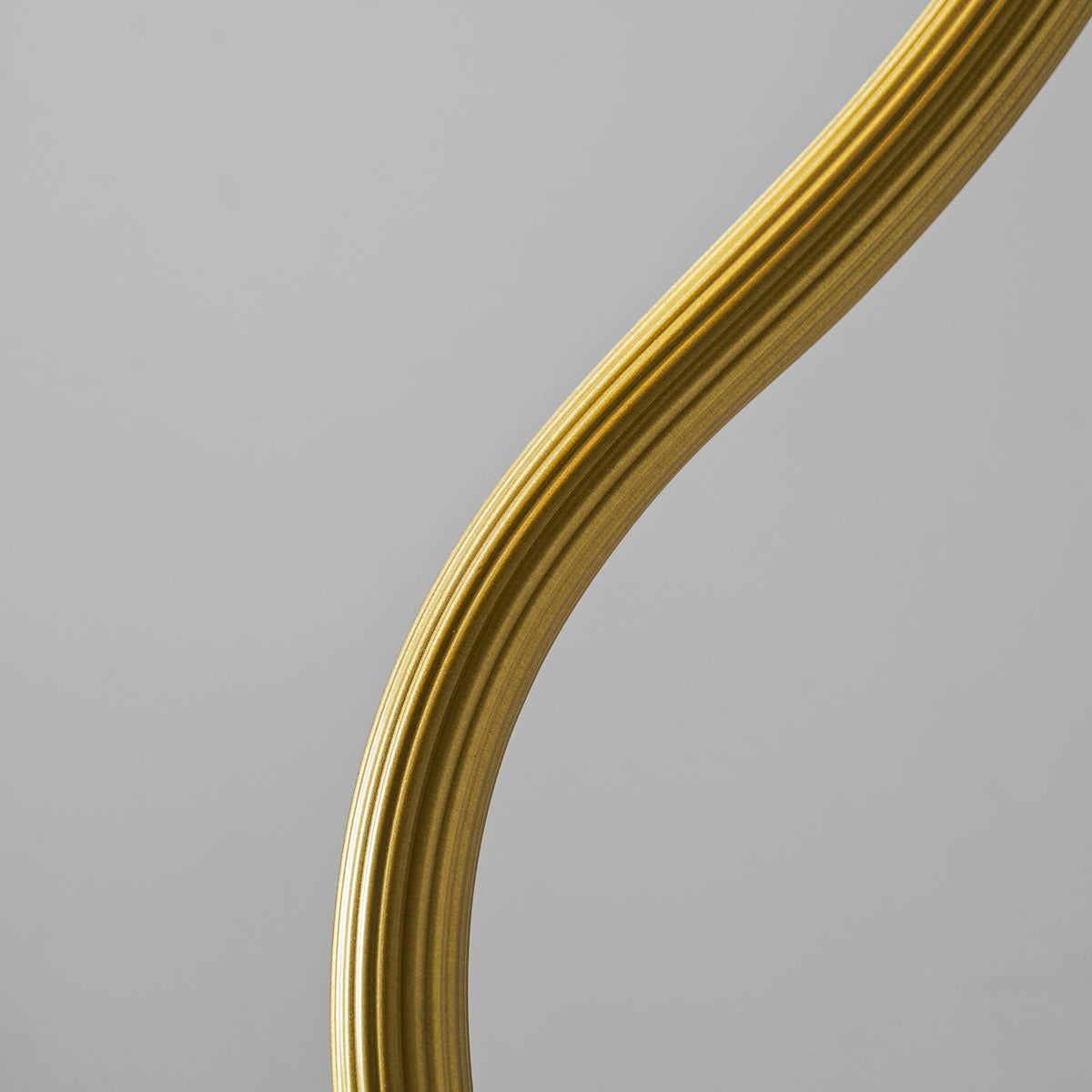 Close view of the ribbed, curving gold arm on this Clérachic lamp against a plain grey backdrop.
