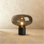 Clérachic larger table lamp with a broad tinted glass shade glowing warm above a black veined marble base