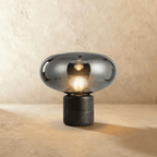 Clérachic larger table lamp in smoky grey glass with a lit globe bulb, on a black veined marble base