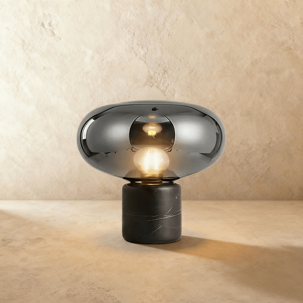 Clérachic larger table lamp in smoky grey glass with a lit globe bulb, on a black veined marble base