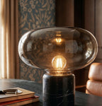 Close view of the Clérachic smoked glass shade, filament bulb and black veined marble base, with a stack of books