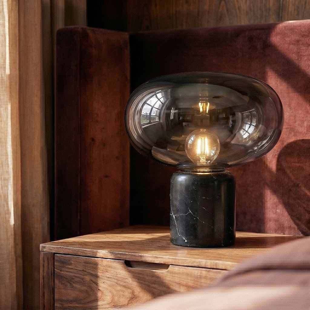 Clérachic table lamp on a walnut bedside table, lit filament bulb under a smoky glass shade, black marble base