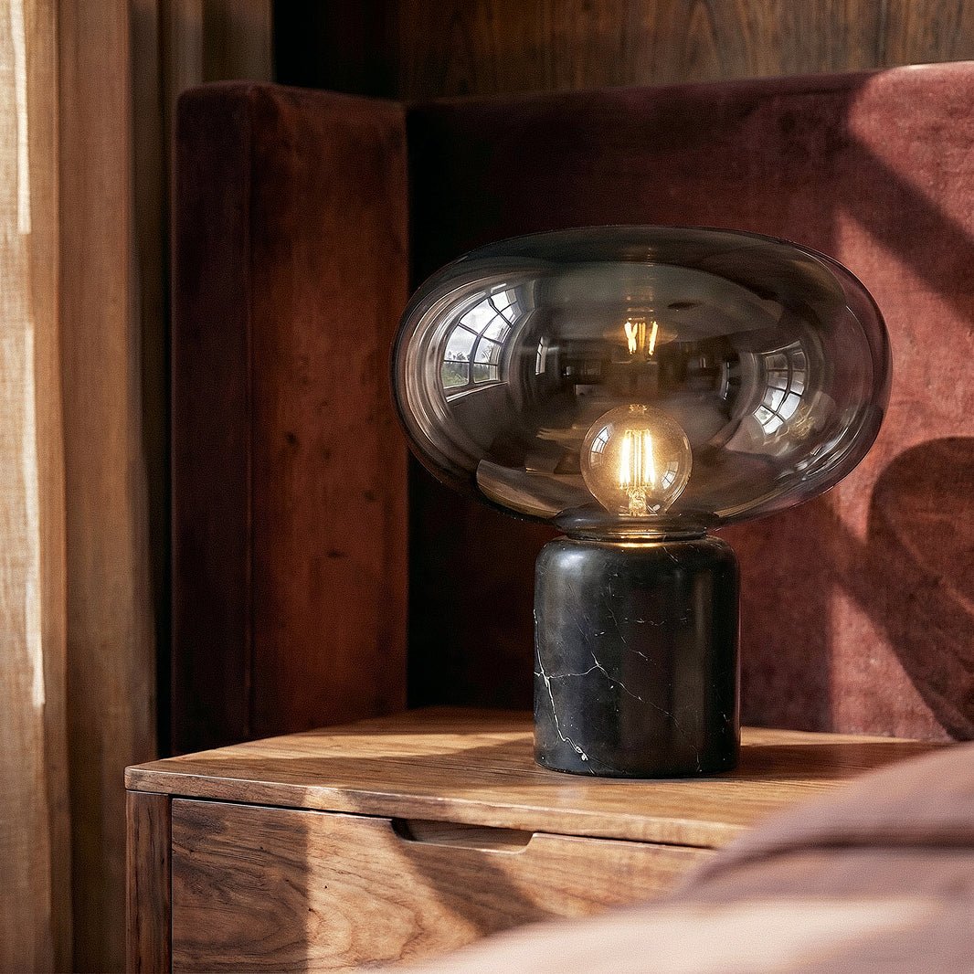 Clérachic table lamp on a walnut bedside table, lit filament bulb under a smoky glass shade, black marble base
