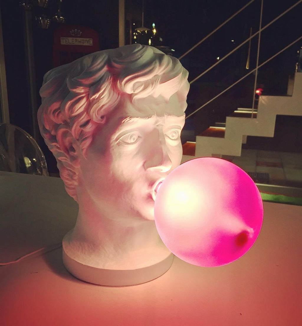 At night, the bubble of this Clérachic bust lamp glows hot pink and lights the white face, with a staircase behind.