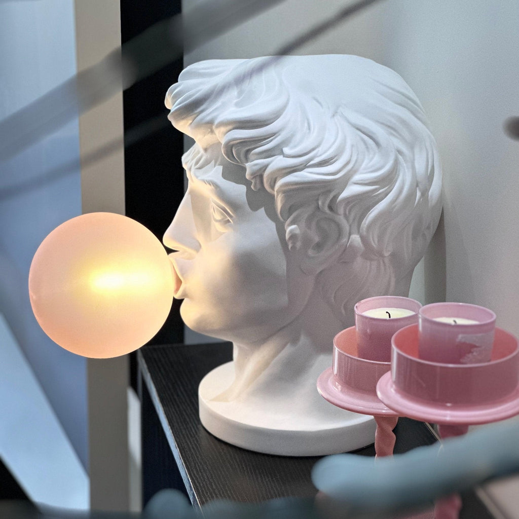 In profile on a dark shelf, a Clérachic white bust lamp blows a softly lit bubble, beside pink tea light holders.
