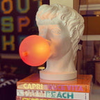 Close view of a Clérachic bust lamp with its bubble lit orange, standing on a pile of travel books.