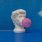 A Clérachic bust lamp with a pink bubble on a vivid blue backdrop and floor, its white cord trailing along the ground.