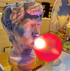Close view of a Clérachic bust lamp with its red-pink bubble lit, the face tinted purple and blue by the light in a shop.