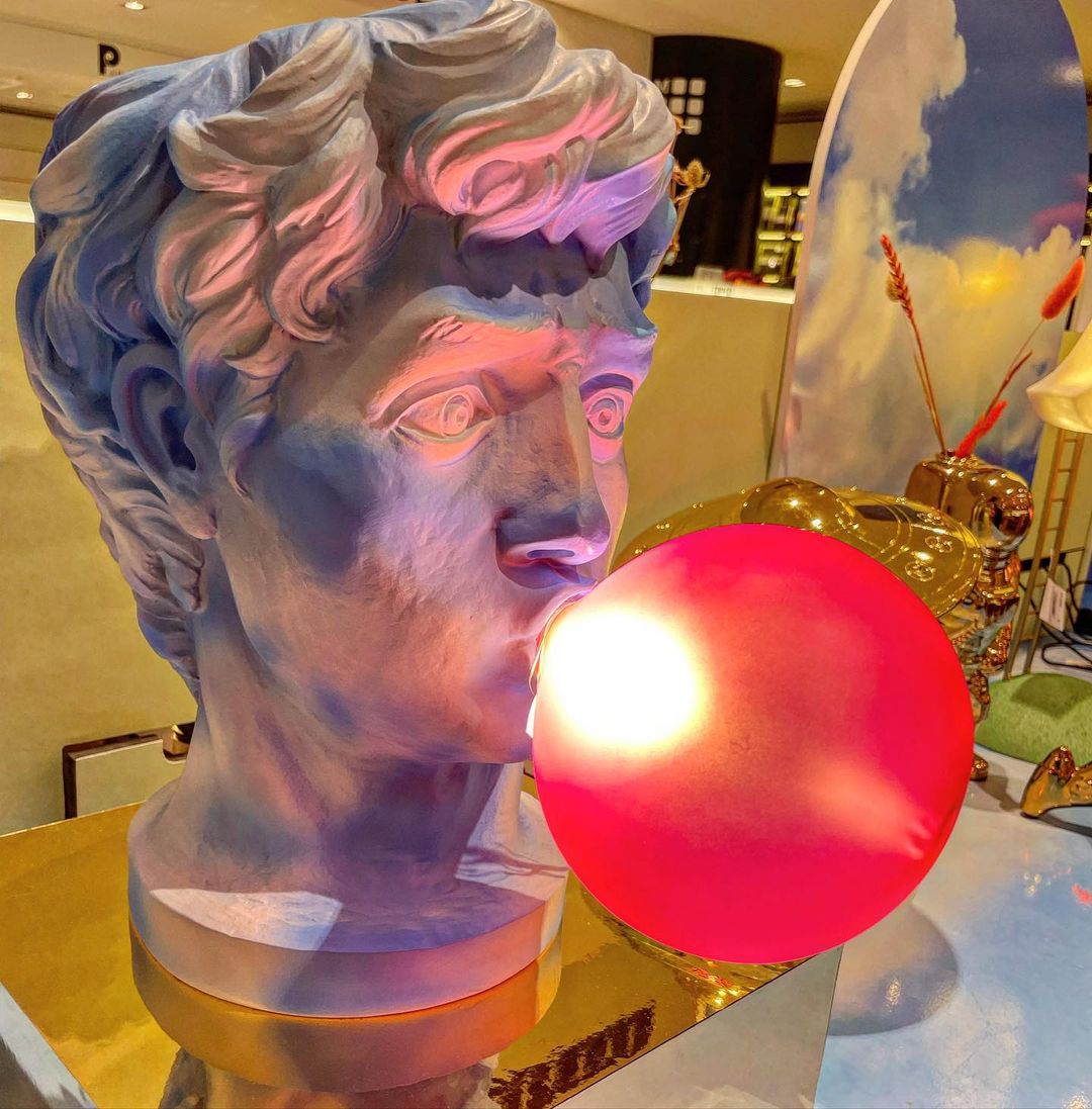 Close view of a Clérachic bust lamp with its red-pink bubble lit, the face tinted purple and blue by the light in a shop.