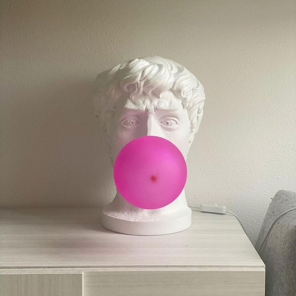 Seen from the front, this Clérachic bust lamp has a bold pink bubble covering the mouth, standing on a pale chest of drawers.