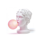 A Clérachic female bust lamp in white, blowing a pale pink bubble, on a plain white backdrop with a thin white cord.