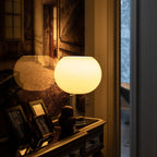 Glowing white glass globe of this Clérachic table lamp on an ornate console, with framed photographs and a moody painted room behind.