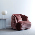A white globe Clérachic table lamp on a clear stem sits on a round side table beside a pink quilted velvet armchair.