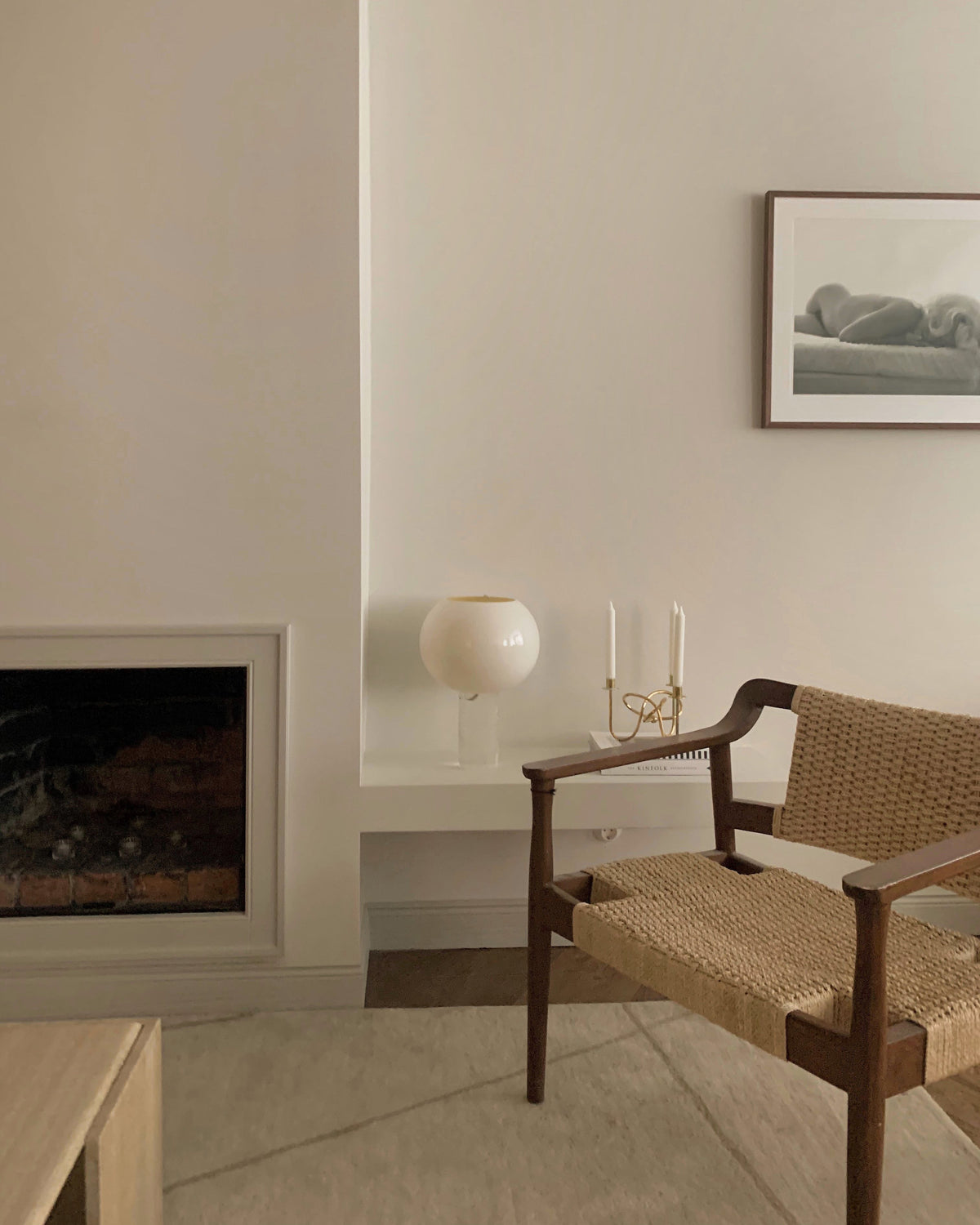 A small Clérachic globe lamp sits on a white ledge beside two candles, near a fireplace and a woven wooden armchair.