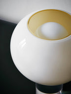 Close view of the white glass globe of this Clérachic table lamp, with its open top showing a soft gold interior and the bulb inside.