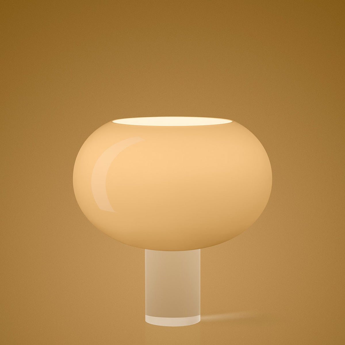 A glowing Clérachic table lamp with a wide, rounded glass shade on a clear cylinder, on a warm gold backdrop.