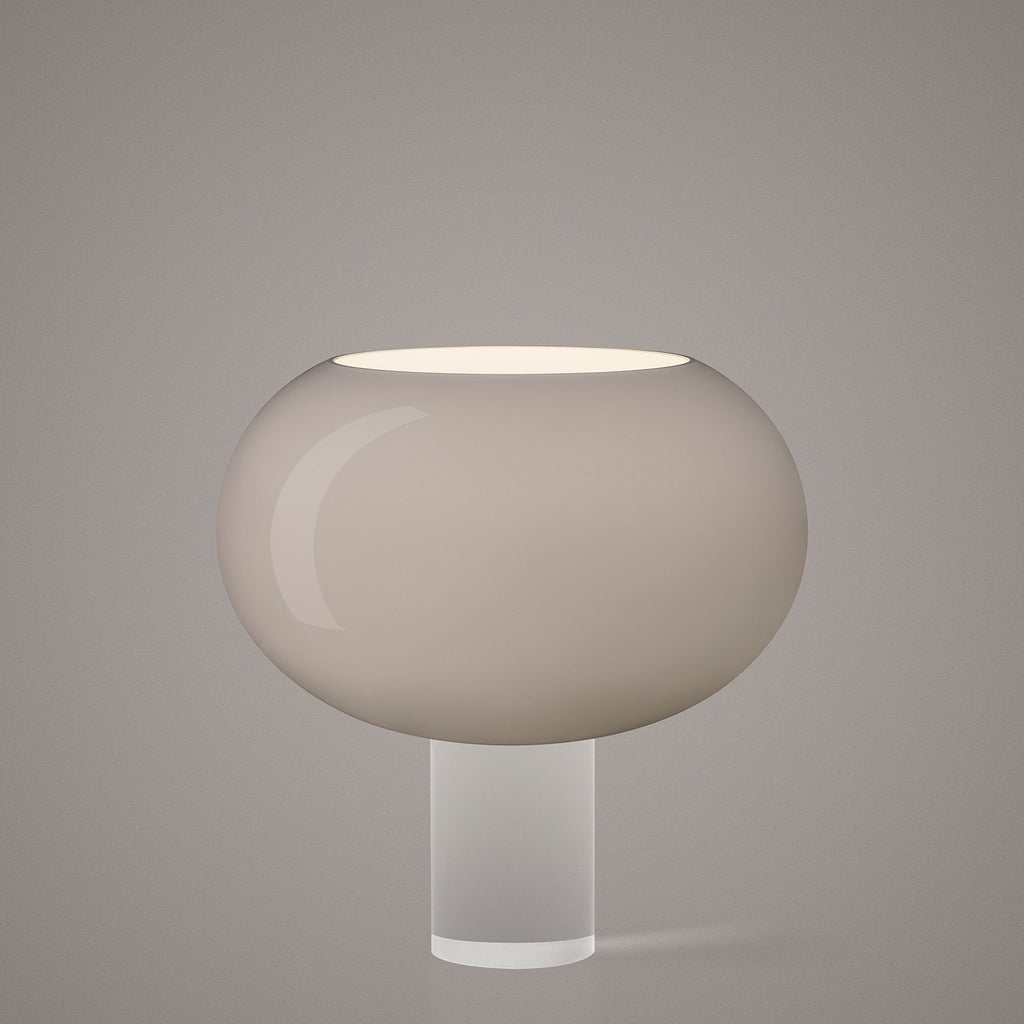 The grey-toned version of this Clérachic table lamp, its wide frosted glass shade on a clear cylindrical base, on a soft grey backdrop.