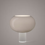 The grey-toned version of this Clérachic table lamp, its wide frosted glass shade on a clear cylindrical base, on a soft grey backdrop.