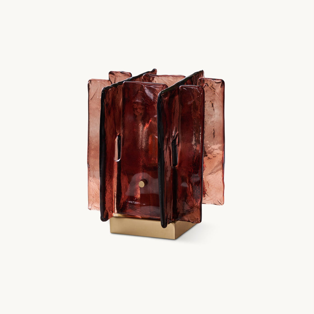 On a plain white backdrop, a Clérachic table lamp with rippled amber-red glass panels standing around a square brushed brass base.