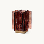 On a plain white backdrop, a Clérachic table lamp with rippled amber-red glass panels standing around a square brushed brass base.