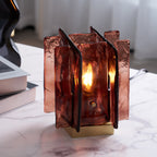 A lit Clérachic table lamp with amber-red glass panels stands on a marble table beside a stack of books and a black vase.