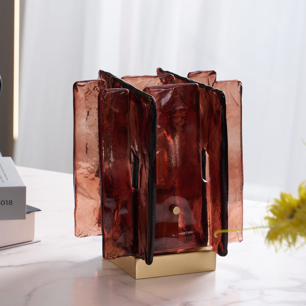Unlit, this Clérachic table lamp shows its translucent amber-red glass panels and brass base on a marble table, with yellow flowers beside it.