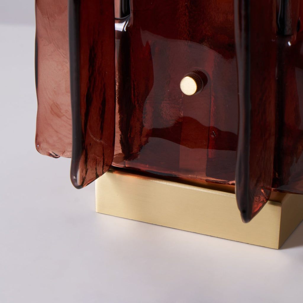 Close view of the base of this Clérachic table lamp, with a small brass pin on a glass panel above its square brushed brass plinth.
