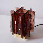 An unlit Clérachic table lamp with amber-red glass panels stands on a pale tabletop, with a black cord leading away to the right.
