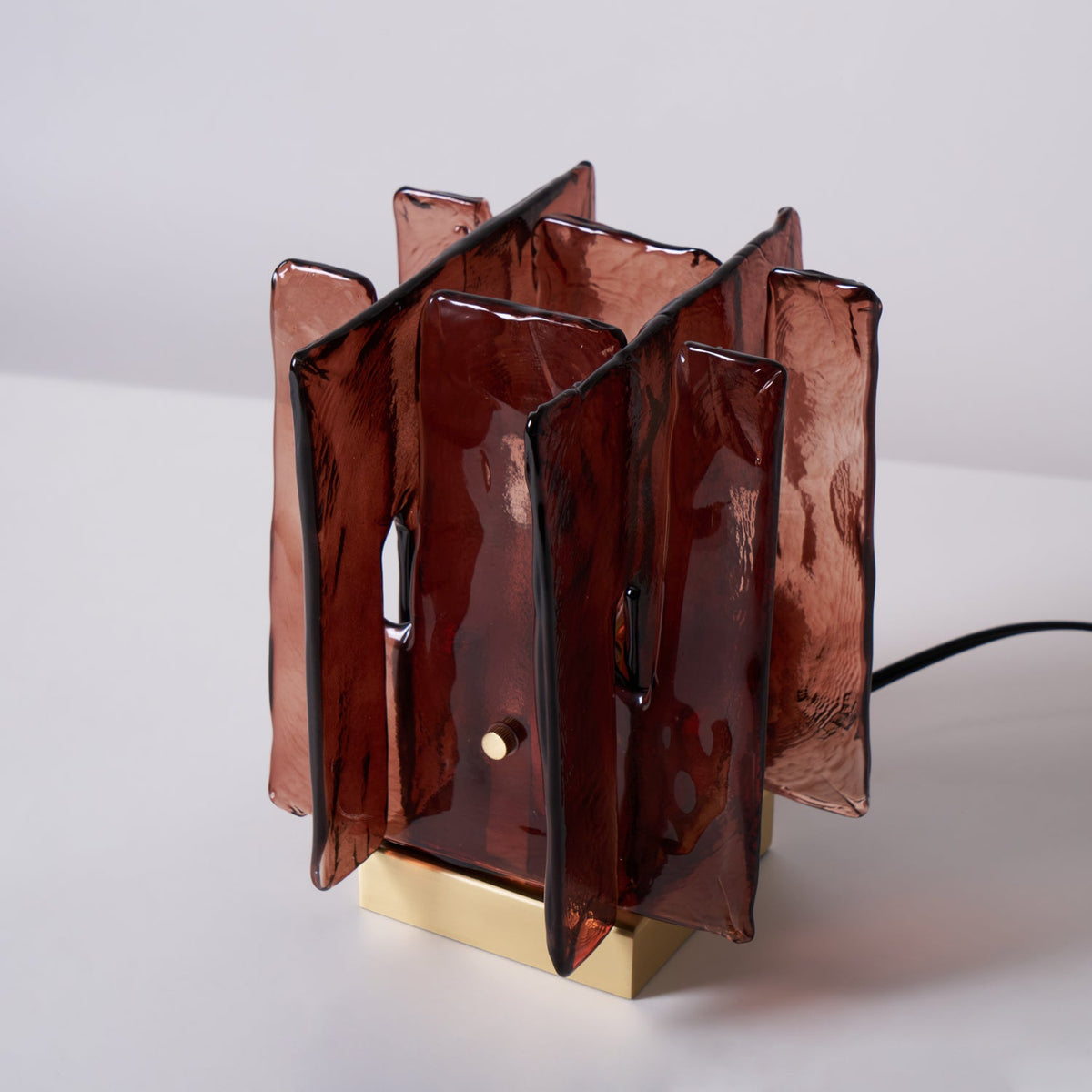 An unlit Clérachic table lamp with amber-red glass panels stands on a pale tabletop, with a black cord leading away to the right.