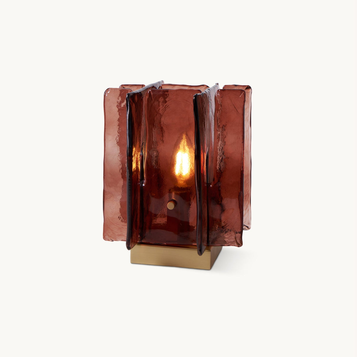 On a plain pale backdrop, a lit Clérachic table lamp shows a candle-style bulb glowing through its amber-red glass panels.
