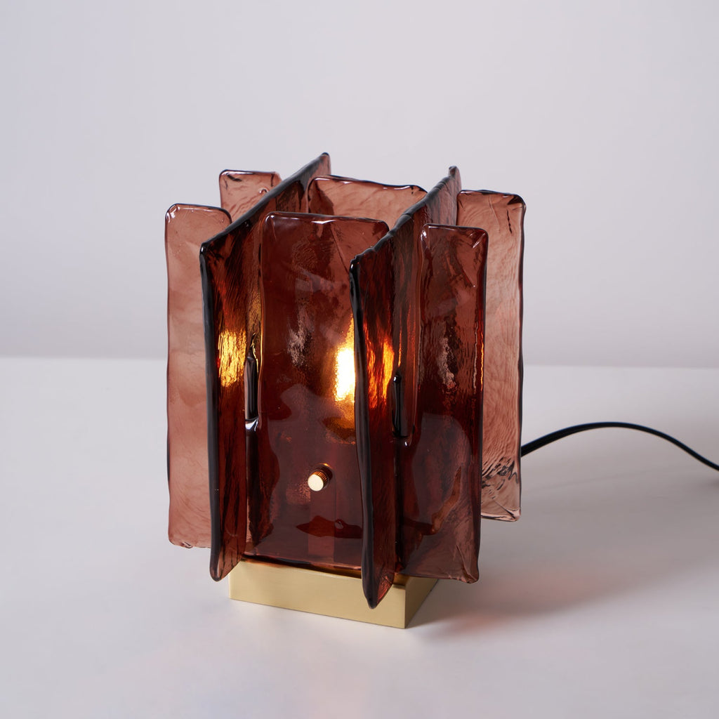 A lit Clérachic table lamp on a pale backdrop, its amber-red glass panels glowing around a candle-style bulb.