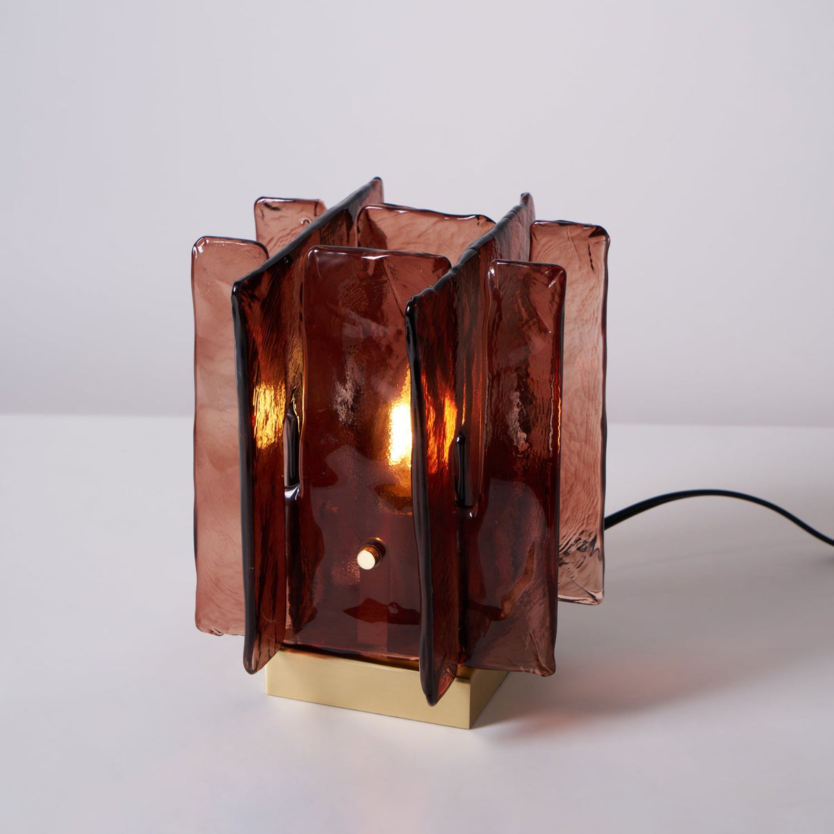 A lit Clérachic table lamp on a pale backdrop, its amber-red glass panels glowing around a candle-style bulb.